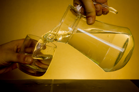 Elegant shot of two hands pouring some water from a pitcher into a glass on a dark backgroundの写真素材