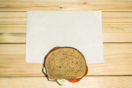 Shot to a vegetarian sandwich made from a few slices of tomato and a few slices of cucumber next to a white plain piece of paper on a wooden backgroundの写真素材