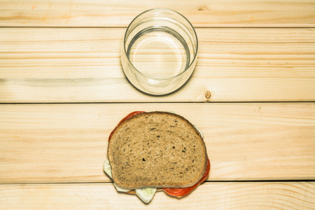 Shot to a vegetarian sandwich made from a few slices of tomato and a few slices of cucumber next to an empty glass on a wooden backgroundの写真素材