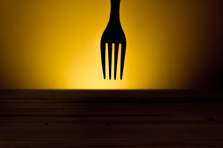 Cutlery silhouette made from a fork on a dark background on top of a wooden tableの写真素材