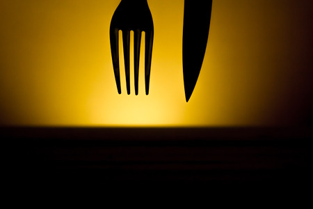 Cutlery silhouette made from a fork and a knife on a dark background on top of a wooden tableの写真素材