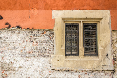 Close up shot to a corroded orange wall texture with bricks and an old window with iron grill and wooden frameの写真素材