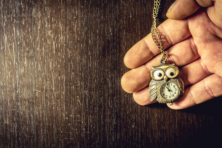 Close up shot to a hand holding an vintage owl watch on a wooden tableの写真素材
