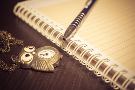 Close up shot to an agenda, a pen and an vintage owl watch on a dark wooden tableの写真素材