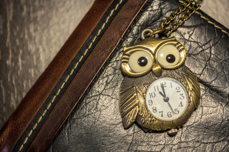 Vintage owl watch sitting on a leather wallet on dark wooden backgroundの写真素材