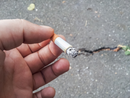 Male hand holding a cigarette with rough asphalt in backgroundの写真素材