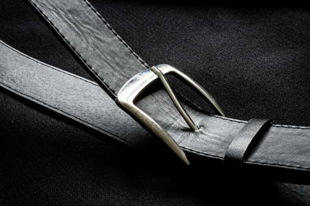 Closeup of a leather belt with metalic buckle near a suit button on a business coat