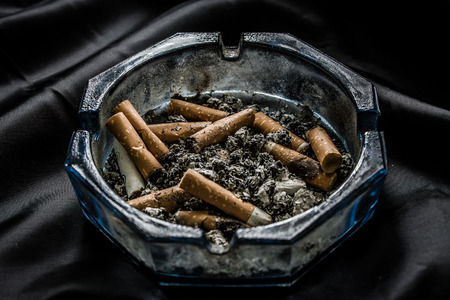 Cigarette butts in ashtray on a dark crumpled silk background