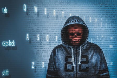 hacker over a screen with binary code and blue lit letters from a keyboardの写真素材