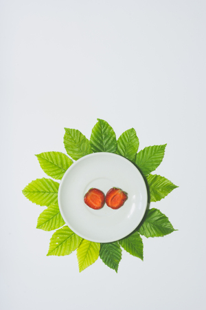 Minimal strawberry slice background. Fruit on white plate with leaves around it. Matte colored. Vertical design for a leaflet, banner, cover or flyerの写真素材