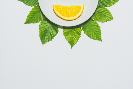 Minimal orange slice background. Fruit on white plate with leaves around it. Matte coloredの写真素材