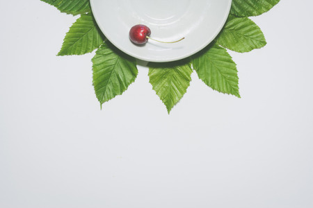 Minimal cherry background. Fruit on white plate with leaves around it. Matte colored.の写真素材