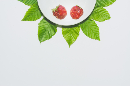 Minimal strawberry slice background. Fruit on white plate with leaves around it. Matte colored.の写真素材
