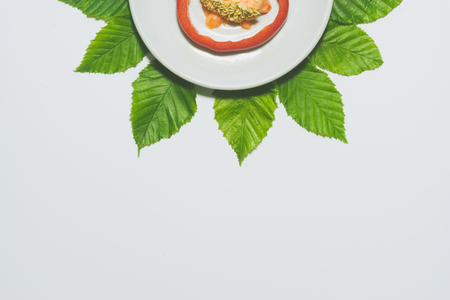 Minimal red pepper slice background. Fruit on white plate with leaves around it. Matte colored.の写真素材