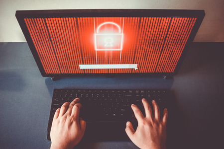 Two hands typing on a keyboard. Locked encrypted data on red screen. Hacking coneptの写真素材