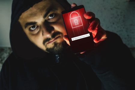 Furious hacker holding a phone with black screen. Cyber attack warning. Ransomware conceptの写真素材