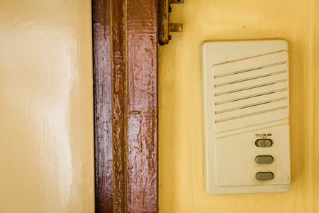 Plastic interphone on yellow wall next to a doorの写真素材