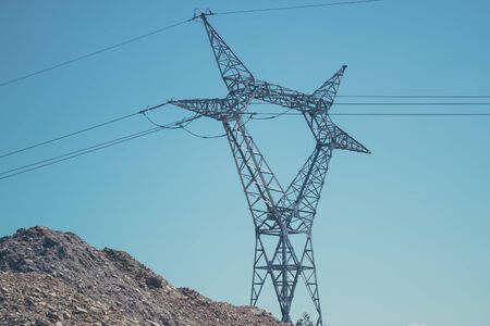 High voltage pole with stretched electric cables over a dirt mound