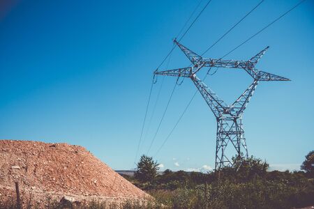 High voltage pole with stretched electric cables over a dirt moundの写真素材