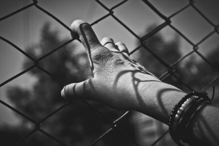 Hand holding on a chain link fenceの写真素材