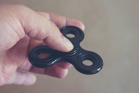 Hand holding fidget spinner against bright background. Finger holding spinning toy. Addictive stress...