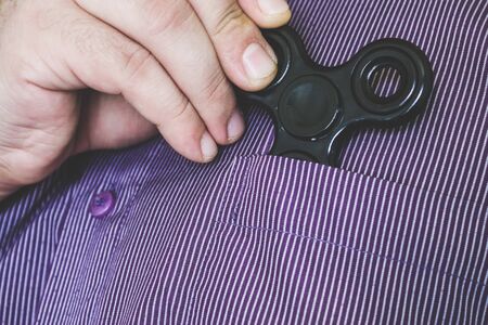 Closeup to a hand pulling out a black fidget spinner out of a shirt pocket. Addictive stress reducer...