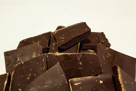 Stack of dark black chocolate pieces on white background with crumbsの写真素材