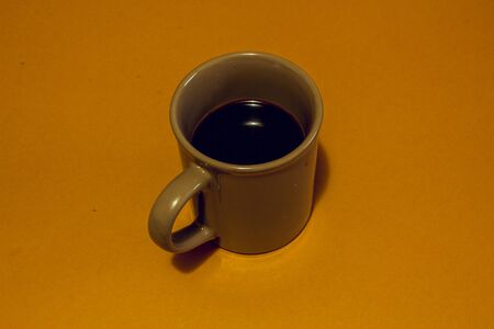 Brown mug with dark strong black coffee in it on a bright caramel color background. Morning concept imageの写真素材