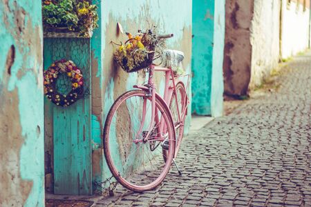 Pink vintage bike with basket full of flowers next to an old cyan building in Spainの写真素材