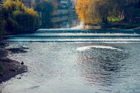 City river flowing over the rocks creating a small cascade. Trees with yellow leaves on the shoreの写真素材