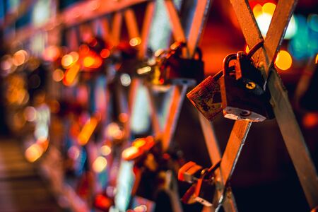 Closeup to a couple of padlocks locked on a bridge illuminated by neon light at nightの写真素材