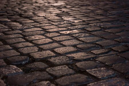Wet illuminated paved road with cobblestone in the nightの写真素材