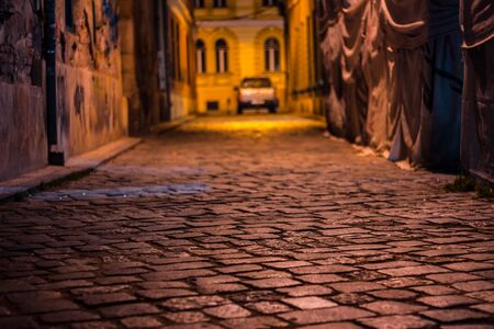 Paved road with cobblestone illuminated by yellow street lights and a car in backgroundの写真素材