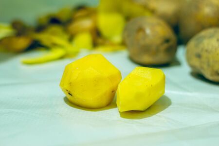 Closeup of peeled potatoes with a pile of unpeeled potatoes on a kitchen tableの写真素材