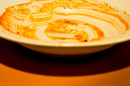 Dirty white plate with dry tomato sauce on it after consuming food on brown backgroundの写真素材