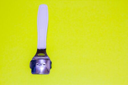Metallic callus remover with a white plastic handle vertically positioned on a light green...