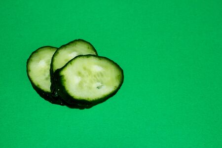Three slices of cucumber on a green background with copy spaceの写真素材