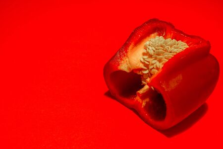 Closeup of a red pepper cut in half with stem and seeds inside clean cut on a red backgroundの写真素材