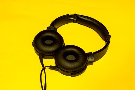 Single black pair of headphones with a thick wire and big headset sponge one a yellow backgroundの写真素材