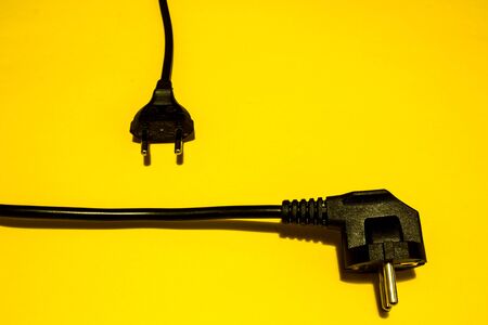 Two types of black unplugged electric plugs on yellow backgroundの写真素材