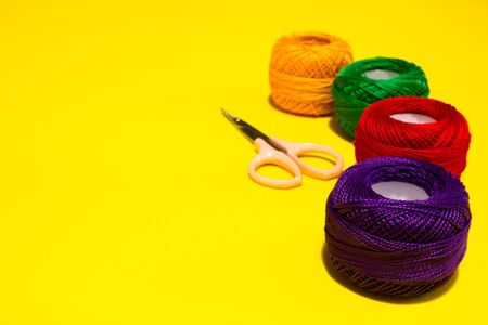 Four wool yarn balls in a row with a small metal pink scissor placed on a yellow background with copy spaceの写真素材
