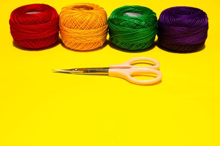 Four wool yarn balls placed in a straight line horizontally on a yellow background near a pink scissor with copy spaceの写真素材