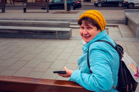 Side view of a senior woman with a big smile on her face sitting on a bench in the park in a cold...