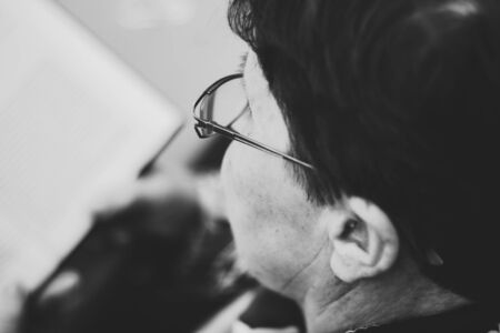 Elder woman with eyeglasses closeup reading a book outdoor â Side view of a beautiful old grandmother sitting on a bench in the park and studying a few pagesの写真素材