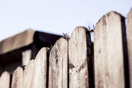 Perspective view of wooden planks and steel cable line with a blurted barn in the background â Closeup of pointy fence with rusty barbed wire on top â Concept background of security and protectionの写真素材