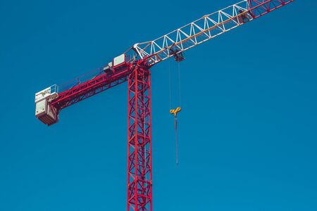 Tall metallic construction equipment with the blue sky in the background â Single industrial device used in architectural purposes â Red and white metallic crane with a yellow hookの写真素材