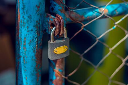 Closed padlock on a chain fence to secure things that are stored behind itの写真素材