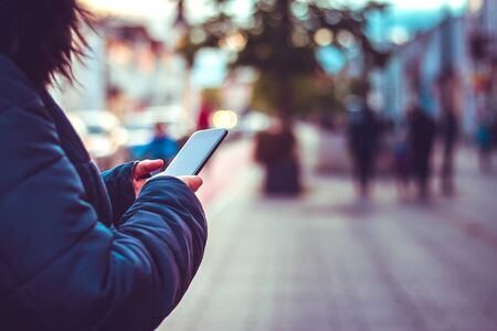 Young woman holding and using a mobile phone outside during a bright day â Big black modern gadget as a frequent mean of communication and socializationの写真素材