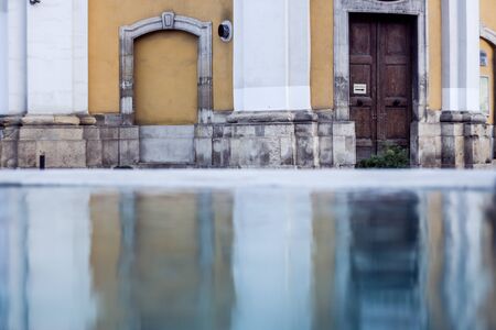 Old yellow building reflection in a rain puddle in the city close after rain â Vintage blurry background with wet street and retro architectureの写真素材