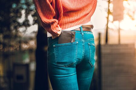 View from behind of a woman wearing tight jeans and an orange blouse with a brown leather wallet placed in the back pocket â Concept image for savings and financesの写真素材